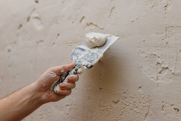 Мужские руки с лопаткой с использованием шпаклевки для стен, строитель делает капитальный ремонт. - Фото, изображение