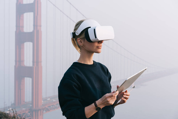 Unrecognizable female artist experiencing virtial reality to draw on digital tablet while standing near Golden Gates in San Francisco alone - 写真・画像