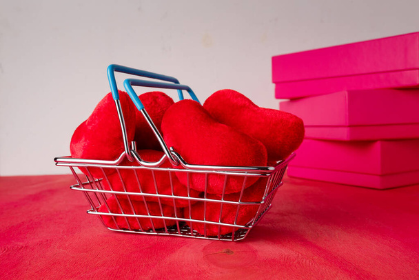 Kırmızı kalpli alışveriş sepeti yumuşak fuayeler, parlak arka planda kutular. Sevgililer günü indirimi, hediyeler. Kart kopyalama alanı - Fotoğraf, Görsel