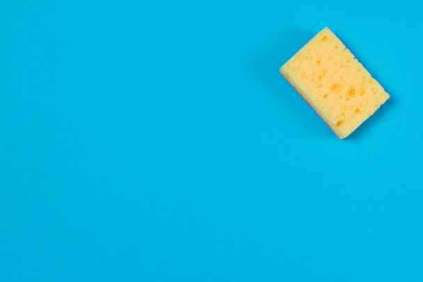 Желтая пористая губка для чистки и мытья посуды на синем фоне с копировальным пространством. Концепция домашнего задания - Фото, изображение