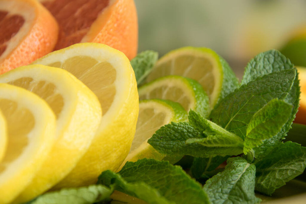 Close-up van bladeren van munt en gesneden sappige citrusvruchten op wazige achtergrond. Snijd sinaasappel, citroen, limoen, grapefruit op bord, rijpe sappige plakjes. Citrusvruchten achtergrond. Zomercitrusvruchten - Foto, afbeelding