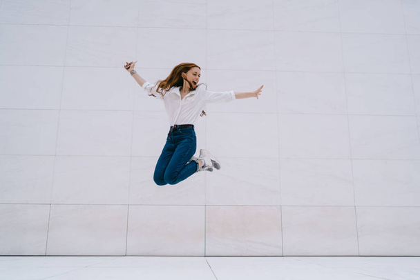 Excited hipster girl in casual apparel feeling satisfied happiness and freedom while jumping near promotional background with copy space area for fashion advertising - Fotoğraf, Görsel