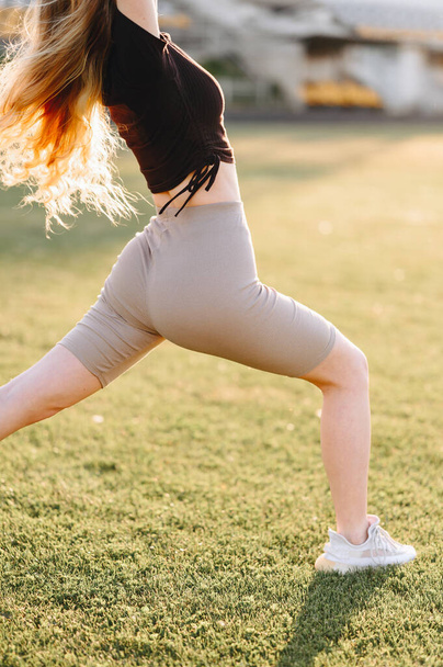 Urheilullinen tyttö syöksyy eteenpäin auringonsäteissä. Urheilullinen pakarat leggingsit lähikuva. Osa liikuntaa luonnossa kesäpäivänä - Valokuva, kuva