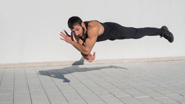 A man in black sportswear jumps while doing push-ups outdoors - Foto, afbeelding