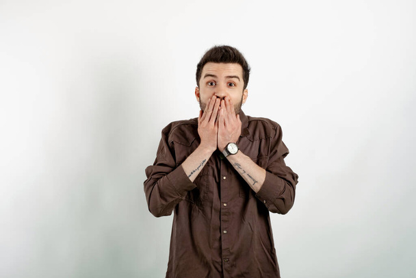 Portrait of young handsome man wearing brown shirt posing isolated over white background shocked covering mouth with hands for mistake while. Secret concept. Looking at the camera. - Foto, Bild