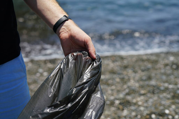 man hand collects garbage on the beach, holds garbage bag. High quality photo - Fotoğraf, Görsel