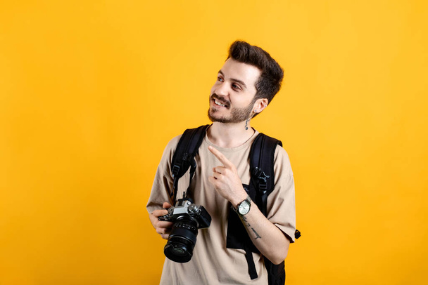Caucasian man wearing beige tee posing isolated over yellow background smiling man pointing left corner with index finger and looking. - Φωτογραφία, εικόνα
