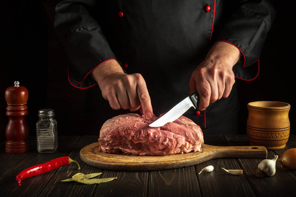 Le mani dello chef con un coltello in cucina tagliano carne cruda. Cucinare cibo delizioso per un ristorante o un hotel - Foto, immagini