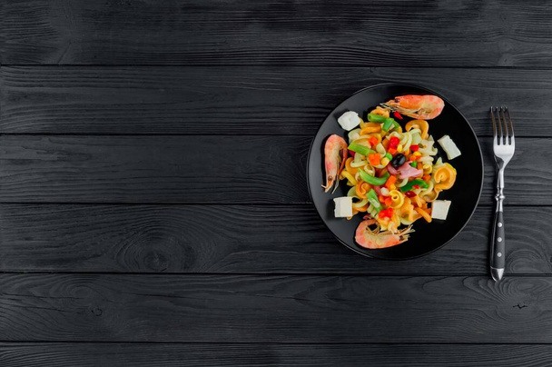 Pâtes multicolores aux crevettes sur fond de bois noir. Servir un plat de pâtes italiennes sur une assiette noire. - Photo, image
