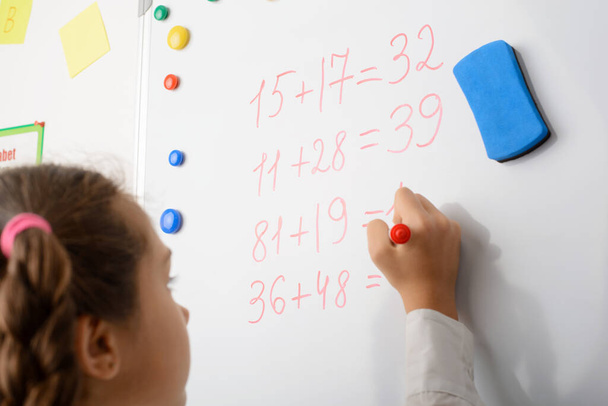 Iskoláslány azzal van elfoglalva, hogy a táblára írjon, számoljon, matekórát vegyen. Az oktatás fogalma - Fotó, kép