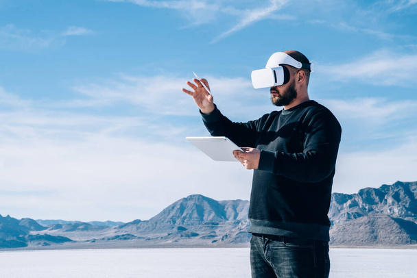 From below of unrecognizable man testing VR headset at Bonneville Salt Flats and using tablet for taking thoughts while traveling around USA - Foto, Imagem