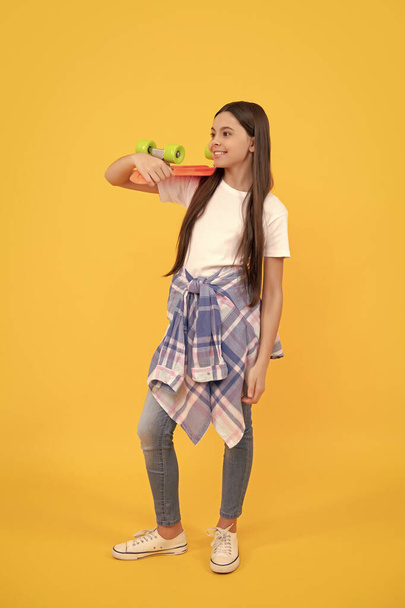 Happy teenager in teen casual holding pennyboard yellow background, board skating. - 写真・画像