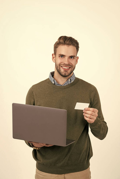 幸せなハンサムな男ビジネスマンは、オンラインで購入し、白に隔離されたオンラインで支払うためのデビットカードとコンピュータを保持します. - 写真・画像