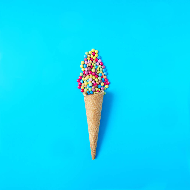 Pastel mavi arka planda küçük renkli çikolatalarla dolu bir dondurma külahı. Yaz tatili ve tatil için en az konsept. Uzayı kopyala Düz yatıyordu - Fotoğraf, Görsel