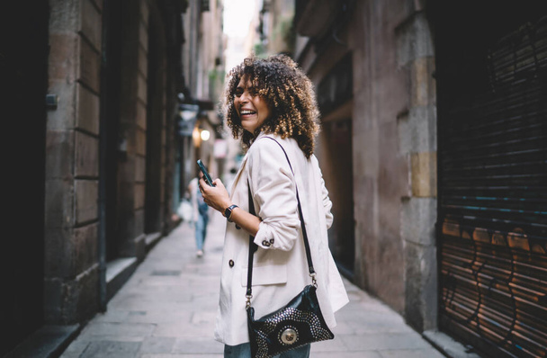  Cheerful millennial blogger with perfect curly hair holding modern smartphone gadget and laughing - Foto, immagini