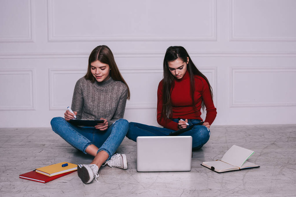 Concentrated female freelancers sitting on floor with crossed legs and clipboards while writing notes and working on project together remotely - Φωτογραφία, εικόνα