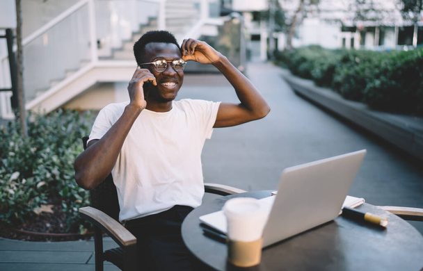 Smiling prosperous dark skinned hipster guy freelance satisfied with international tariffs and connection during remote job on cafe terrace, - Фото, зображення