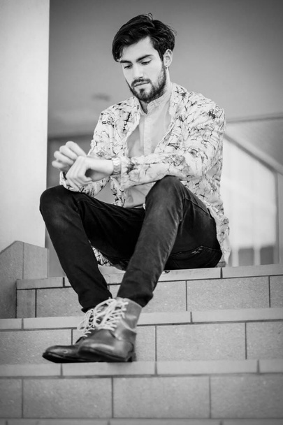 handsome Italian dark-haired guy sitting on white stairs. High quality photo - Фото, изображение