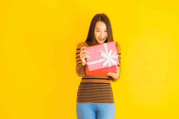 Portré gyönyörű fiatal ázsiai nő boldog mosoly piros ajándék doboz sárga elszigetelt háttér - Fotó, kép