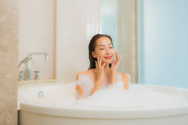 Portrait belle jeune femme asiatique se détendre sourire dans la baignoire à l'intérieur de la salle de bain - Photo, image