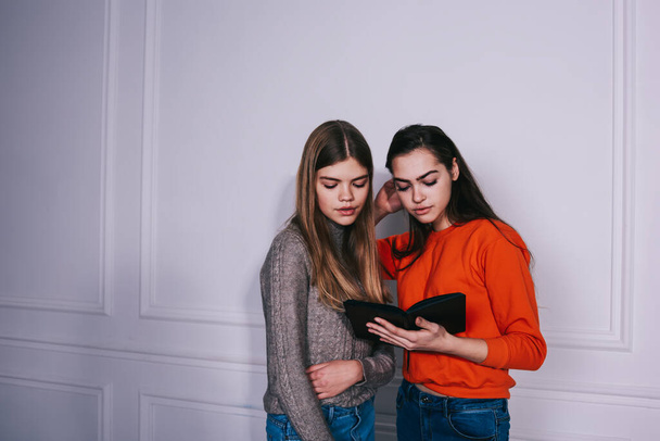 Young focused long haired female students in casual clothes reading textbook together while preparing for exam standing in light lounge - Foto, imagen