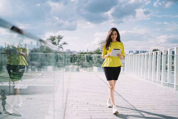 Cheerful asian woman in sporty casual wear walking with digital tablet reading income messages and blog - Fotó, kép