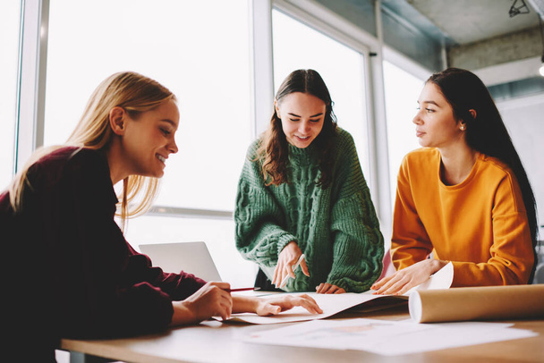 Low angle of female coworkers in casual clothes collaborating while working on new project together standing near table with papers - Foto, Imagen