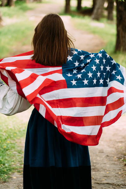 Жінка з національним прапором США стоїть на відкритому повітрі в літньому парку. Позитивна дівчина, яка відзначає День незалежності США. - Фото, зображення