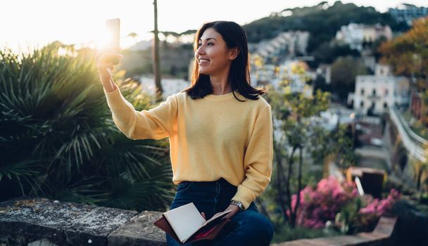 Asiatisches Hipster-Mädchen mit Bildungslehrbuch mit Handy-Kamera zum Klicken von Landschaftsbildern während des Urlaubs - Foto, Bild