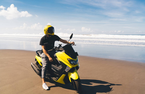 Unrecognizable biker in casual wear and helmet with stylish motorbike enjoying freedom while riding at seaside on sunny summer day - Foto, imagen
