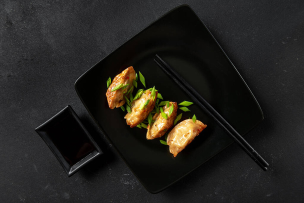 Gyoza - traditional Asian or Japane food on a black background with chopsticks and soy sauce, top view - Фото, изображение