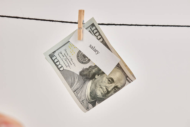 Een $100 biljet met het woord "salaris" hing aan een waslijn. - Foto, afbeelding