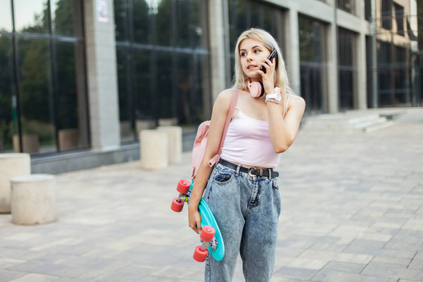 Cool young girl with skateboard talking on phone in the city - Фото, зображення