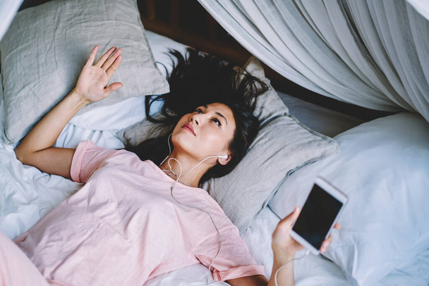 Millenniumi hipster lány alsónadrágban fekszik otthon gyöngy és hallgat audio könyv vasárnap reggel kényelmes lakás - Fotó, kép