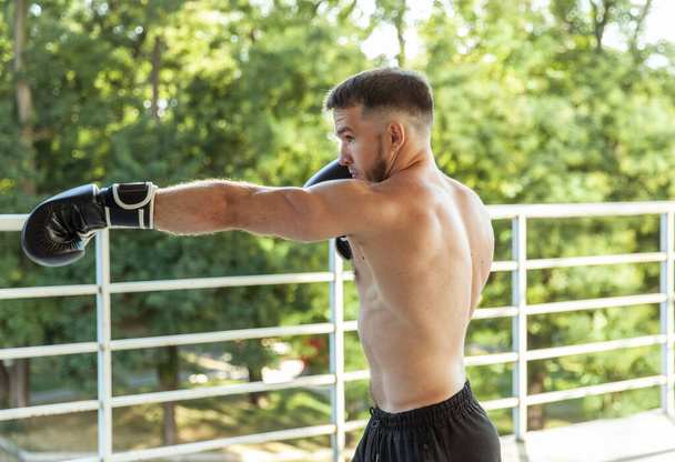 Muscular man training punches with boxing gloves outdoors - Foto, Imagem