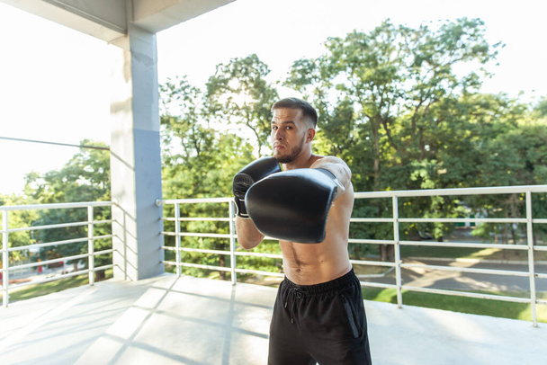 Muscular man training punches with boxing gloves outdoors - Zdjęcie, obraz