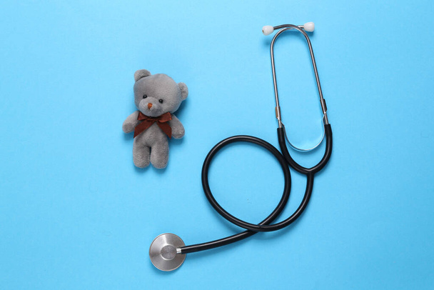 Stethoskop mit Teddybär auf blauem Hintergrund. Konzept der Kindermedizin. Ansicht von oben - Foto, Bild