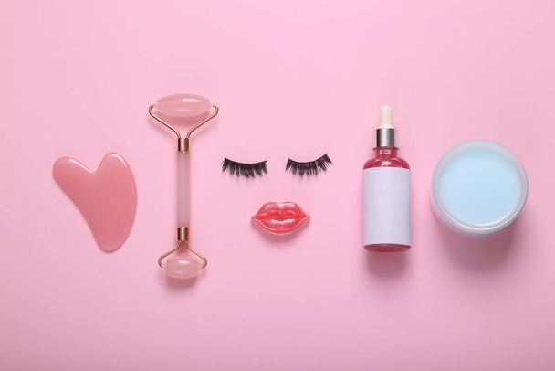 Gezicht van wimpers en lippen met cosmetica en gezichtsverzorging producten op een roze achtergrond. Schoonheid plat lay - Foto, afbeelding