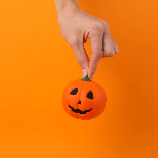 Рука держит антистрессовую игрушку в виде головы тыквенного фонаря на оранжевом фоне. Концепция Хэллоуина - Фото, изображение