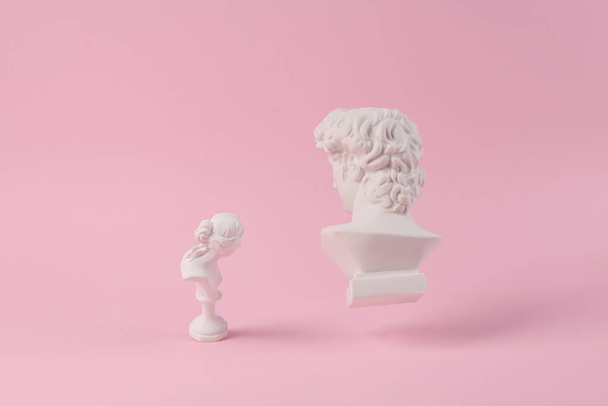 Levitáló antik vakolat mellszobrok David és Vénusz rózsaszín háttérrel árnyék. Fogalmi pop. Minimális csendélet fotózás - Fotó, kép