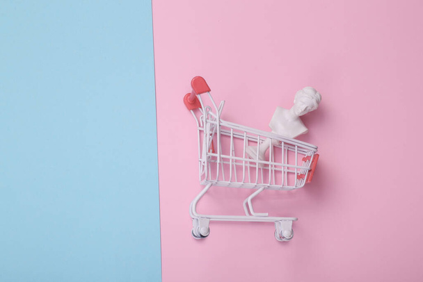 Shopping trolley with venus bust on pink blue background. Creative layout. Minimal shopping still life. Flat lay. Top view - Valokuva, kuva