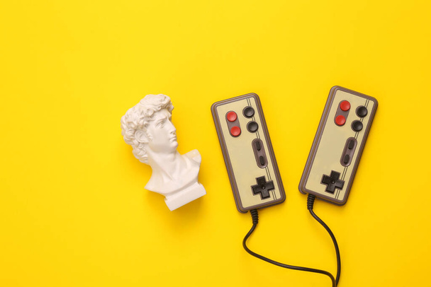 Retro gamepads with David bust on yellow background. Gaming. Creative layout. Minimal still life. Flat lay. Top view - Photo, Image