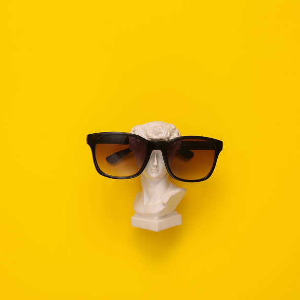 Minimal still life. Antique David bust with sunglasses on yellow background. Summer rest - Photo, Image