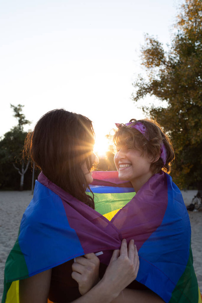 jong lesbisch paar knuffelt teder. regenboogvlag op straat. gelijke rechten voor de Igbt gemeenschap, intimiteit en gevoelens voor twee meisjes - Foto, afbeelding