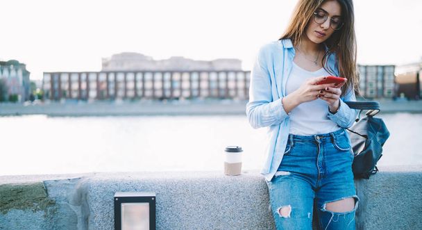 Millennial woman reading incoming notification on modern smartphone device mailing at embankment - Фото, изображение