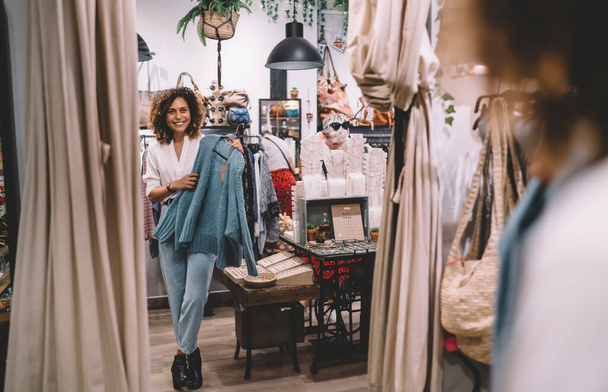 Cheerful hipster girl posing near glass looking at own reflection while choosing brand clothing on shopping - Foto, Imagen