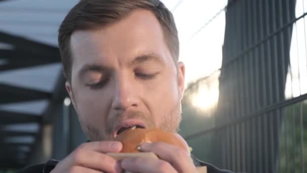 Nälkäinen toimistopäällikkö syö herkullista hampurilaista. Haitallista pikaruokaa. 4k-video - Materiaali, video