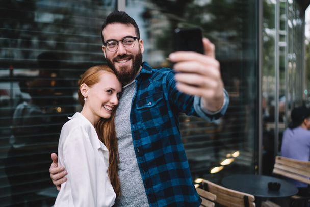 Millennial girlfriend and boyfriend in optical spectacles smiling at front cellphone camera while making positive media content - Φωτογραφία, εικόνα