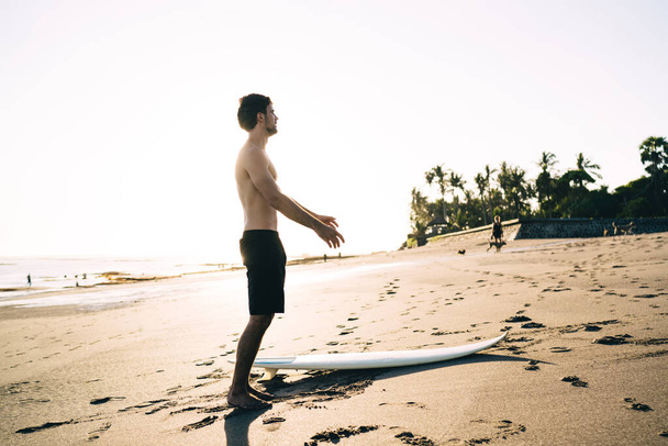 Young male surfer spending free daytime for practice favourite water hobby standing at Carribean beach,  - 写真・画像