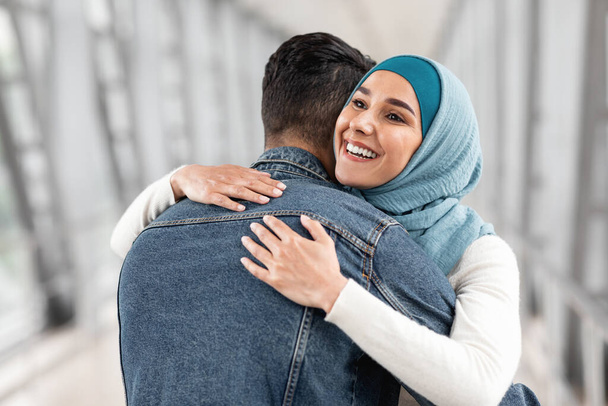 Feliz Reunión. Mujer musulmana alegre en Hijab abrazando a su marido en el aeropuerto después de la llegada del vuelo, emocionada de ver a su cónyuge, joven pareja islámica abrazando en la terminal, primer plano disparado con espacio de copia - Foto, Imagen
